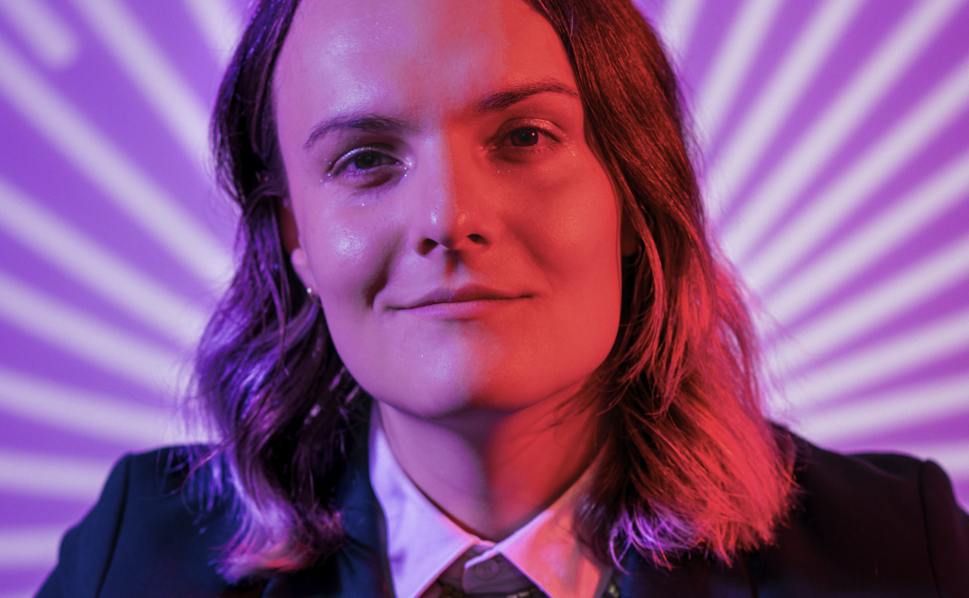 Lux looks just beyond the camera, framed in red and purple lights over a starburst background.