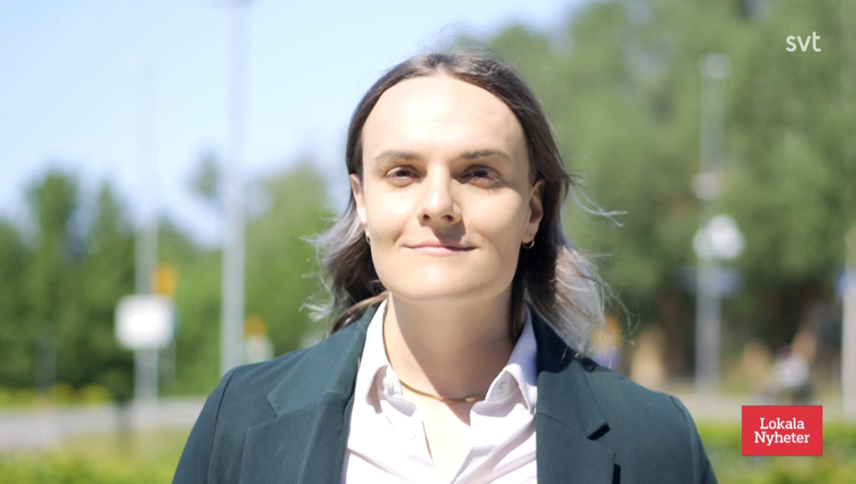 Lux stands in the way-too-bright direct sunlight in a crisp collared shirt and blazer.